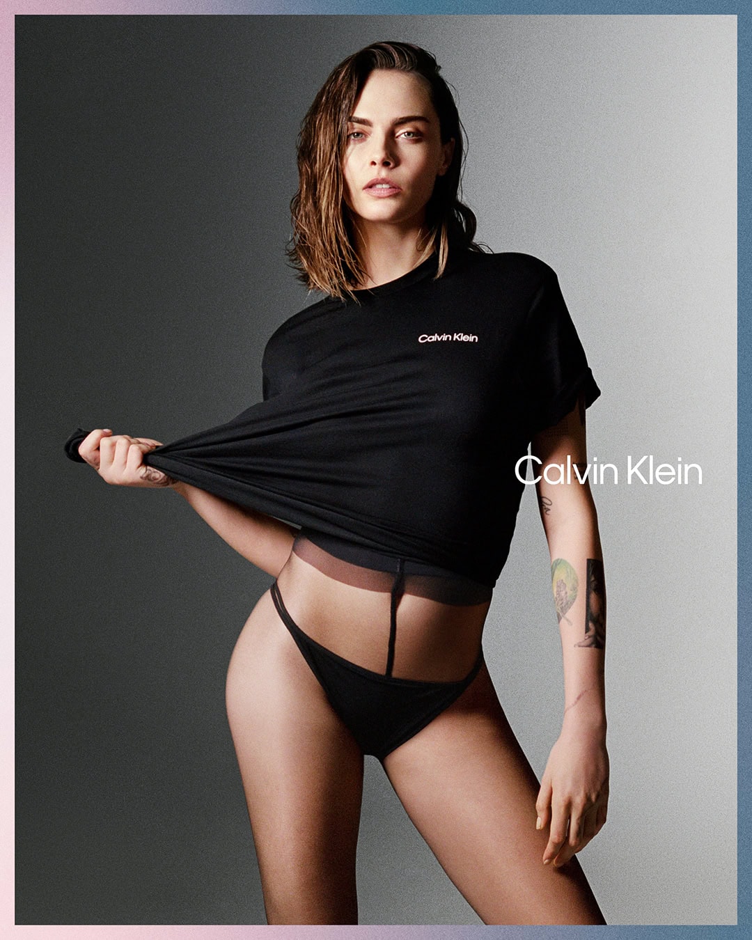 Fashion shot of Cara Delevingne in black top and underwear, posing against gradient grey background with Calvin Klein branding. 