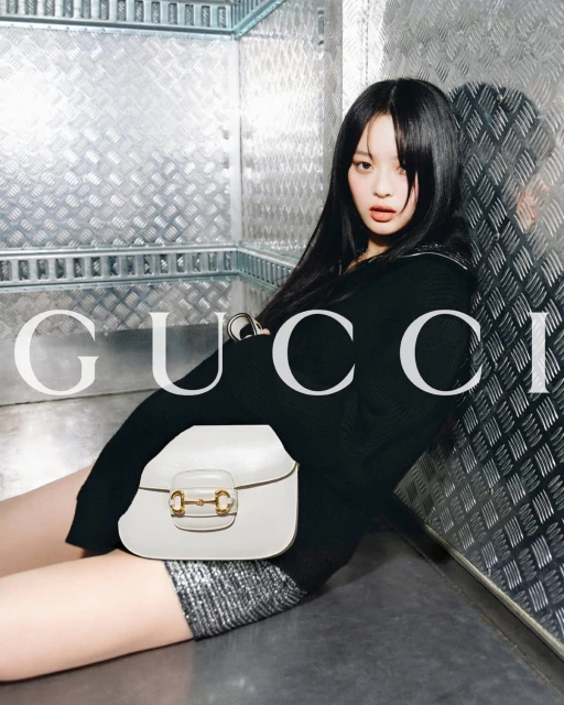 Elegant Asian woman poses with a Gucci purse in a metallic setting, showcasing a blend of fashion and urban style. The image highlights the purse.