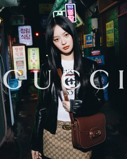 A young woman poses in an alleyway with neon signs, wearing a Gucci top, jacket, skirt, and handbag, showcasing a fashion-forward aesthetic.