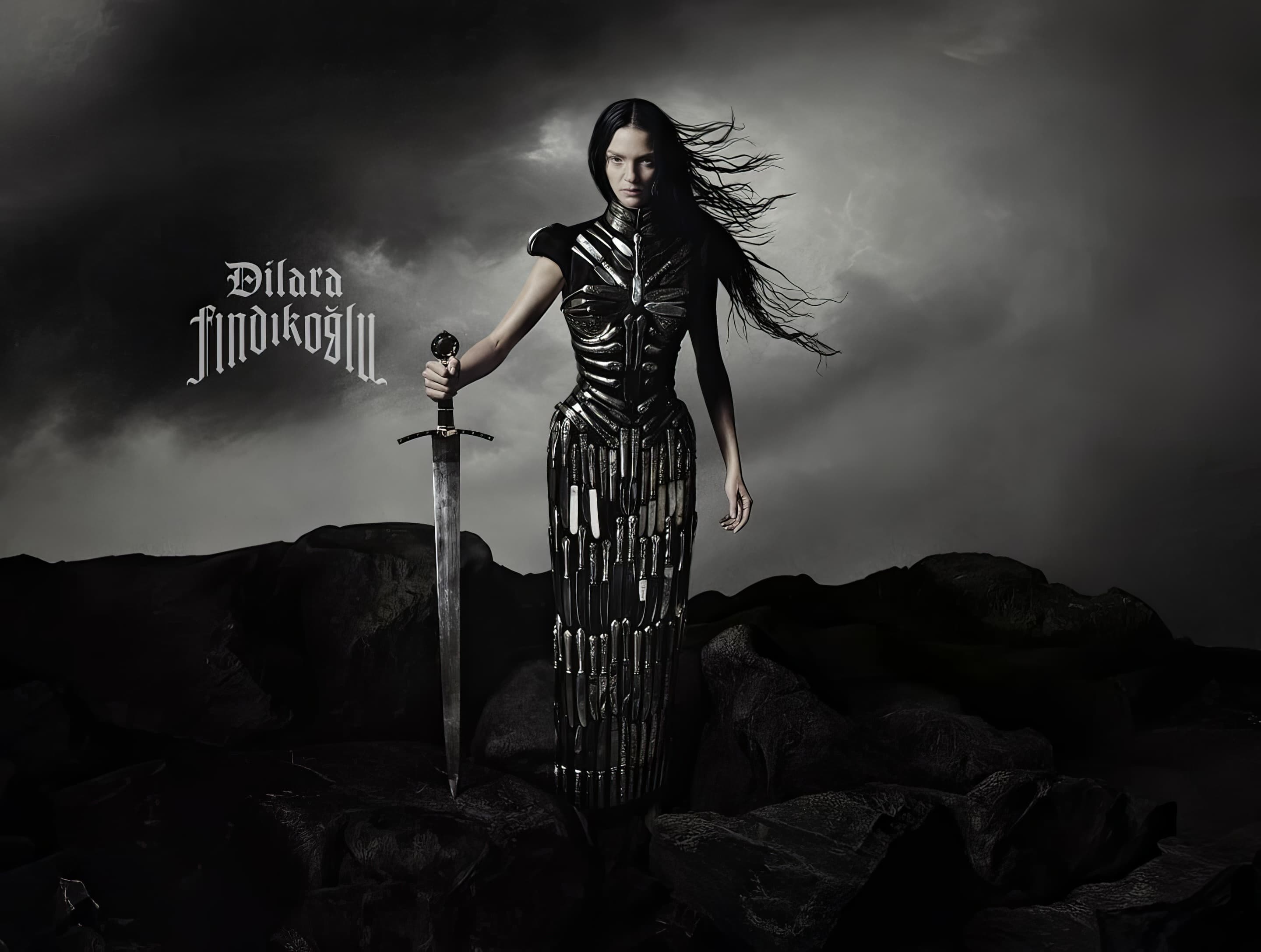 A woman in a dress made of knives stands holding a sword on a rocky landscape with dramatic lighting and cloudy skies in the background.