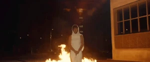 Woman in white hooded dress standing before a street fire at night for Marcia Spring 2024 ad campaign