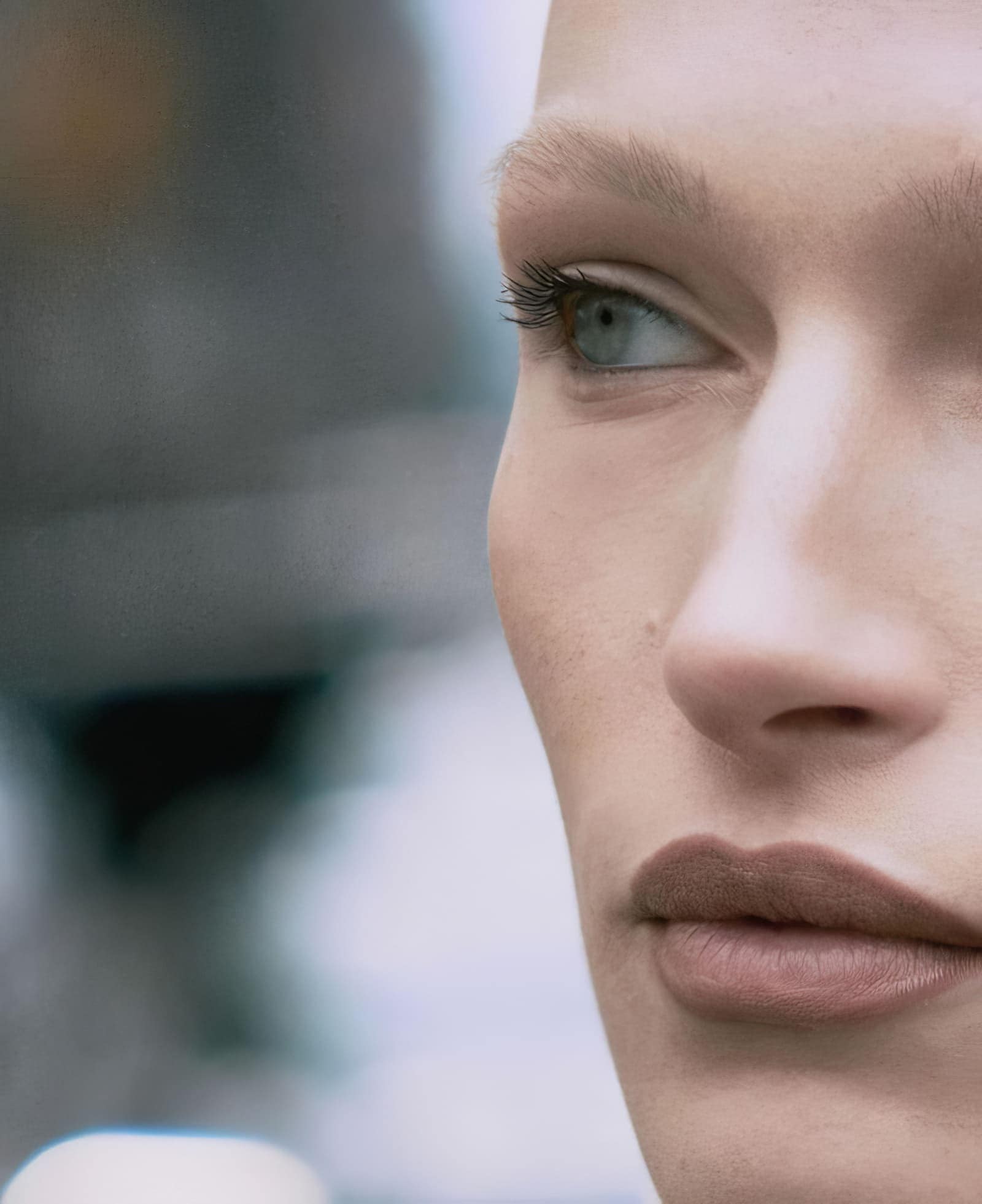Close-up portrait of a fair-skinned adult female model with light eyes, nude lipstick, and blonde eyebrows and eyelashes.