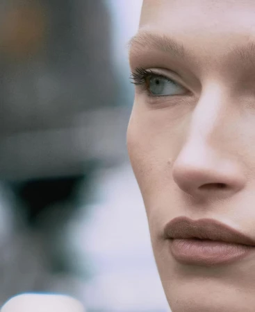 Close-up portrait of a fair-skinned adult female model with light eyes, nude lipstick, and blonde eyebrows and eyelashes.