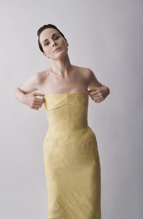 Michelle Dockery wearing a yellow strapless paneled dress against a neutral grey studio background for Emilia Wickstead.