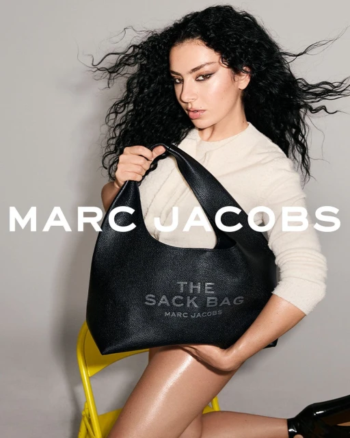 Fashion shot featuring a woman with dark curly hair holding a black Marc Jacobs handbag while sitting on a yellow chair in studio.