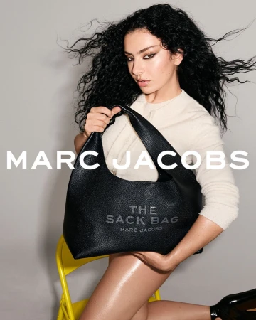Fashion shot featuring a woman with dark curly hair holding a black Marc Jacobs handbag while sitting on a yellow chair in studio.