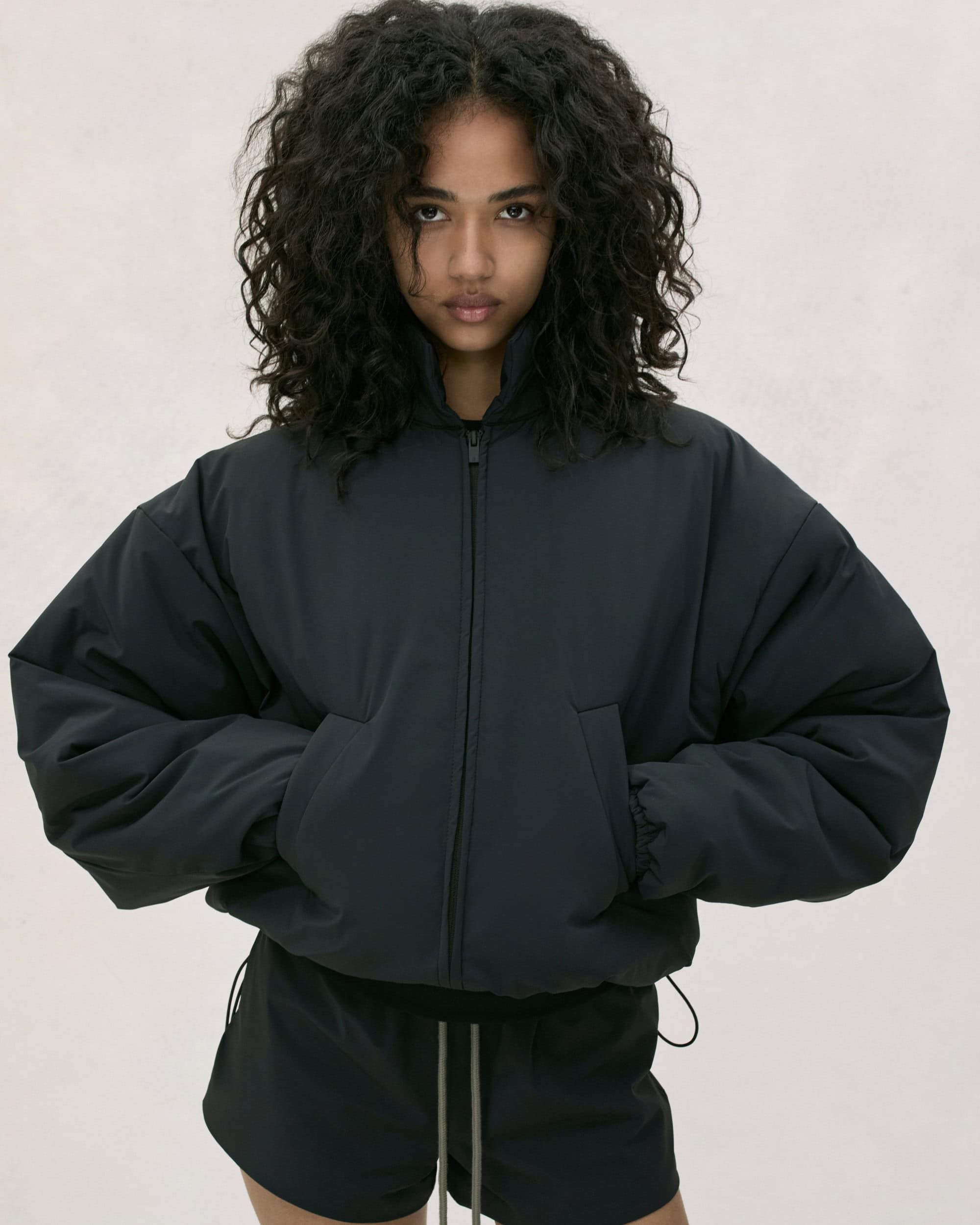 Model with dark curly hair wearing a dark zip-up jacket against a light backdrop for Fear of God