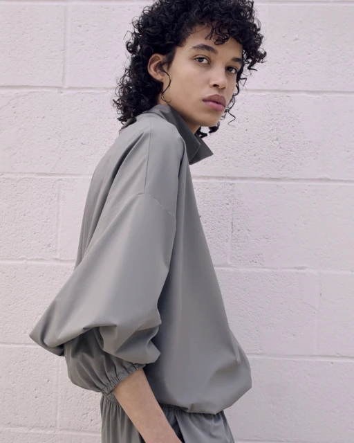 Fashionable adult with curly hair poses in a studio wearing a contemporary grey-green matching top and pants for a fashion shoot.