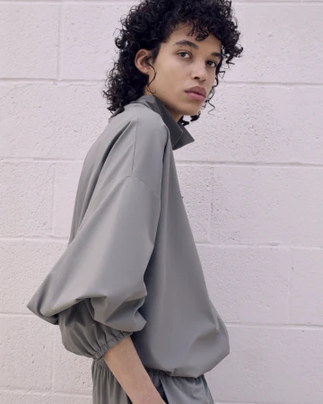 Fashionable adult with curly hair poses in a studio wearing a contemporary grey-green matching top and pants for a fashion shoot.