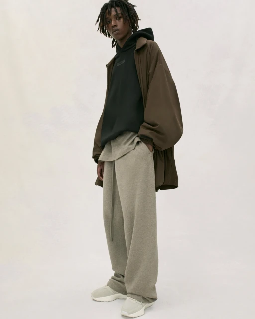 A person models brown wide-leg pants, sweatshirt, hoodie and jacket in a studio. The lighting is soft and neutral with a white background.