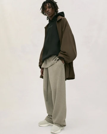 A person models brown wide-leg pants, sweatshirt, hoodie and jacket in a studio. The lighting is soft and neutral with a white background.
