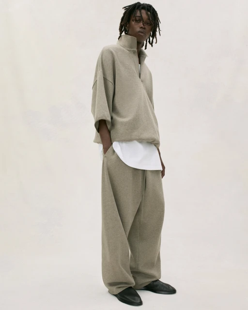 Fashion portrait of adult male model wearing beige quarter-zip sweatshirt and sweatpants with black shoes in a neutral studio setting.