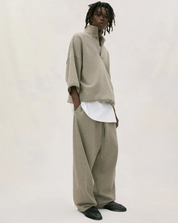Fashion portrait of adult male model wearing beige quarter-zip sweatshirt and sweatpants with black shoes in a neutral studio setting.