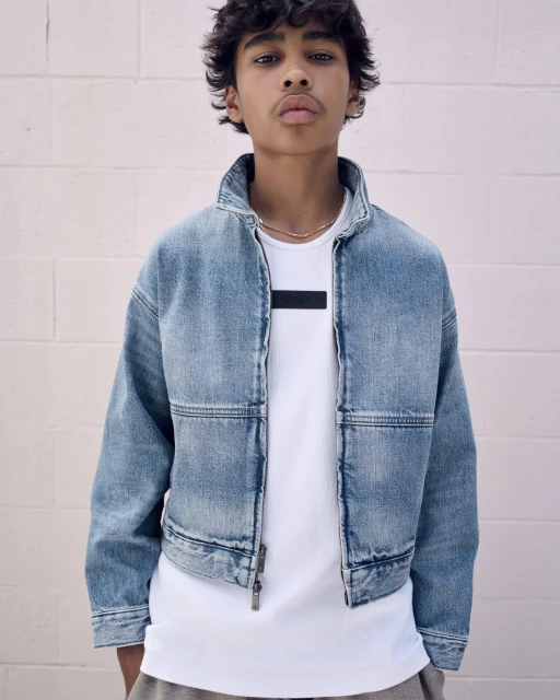 Teenager in a denim jacket and white t-shirt posing in front of a pink wall, showcasing a casual and modern fashion look.