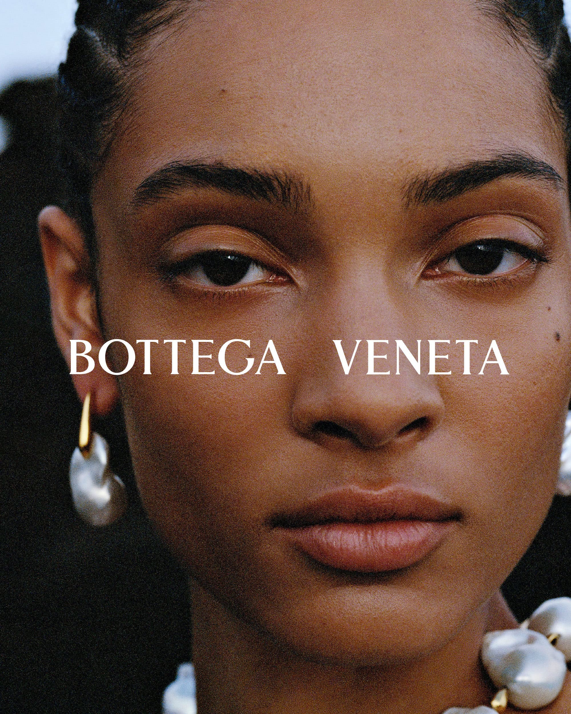 Close-up shot of an adult Black woman with pearl earrings and a pearl necklace, featuring prominent 'BOTTEGA VENETA' text overlay.
