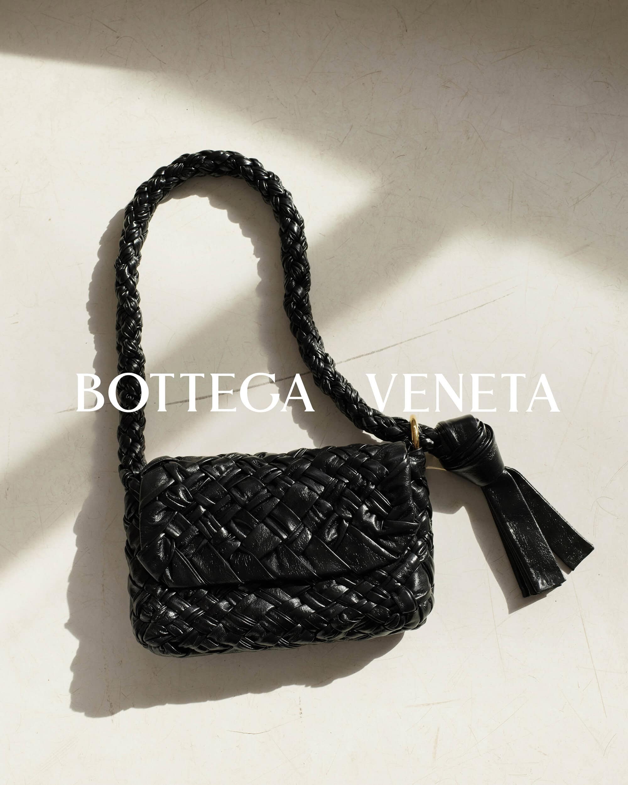 Close-up of a black Bottega Veneta woven shoulder bag with a short, braided strap, featuring a tassel detail and textured surface.