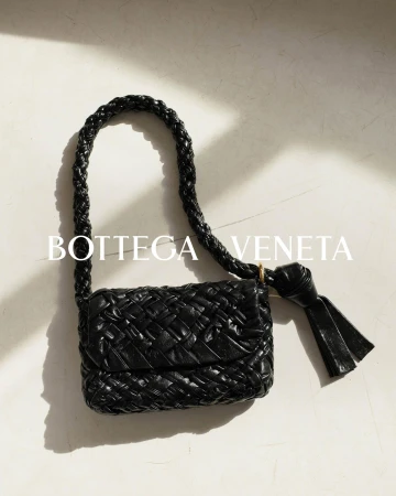 Close-up of a black Bottega Veneta woven shoulder bag with a short, braided strap, featuring a tassel detail and textured surface.