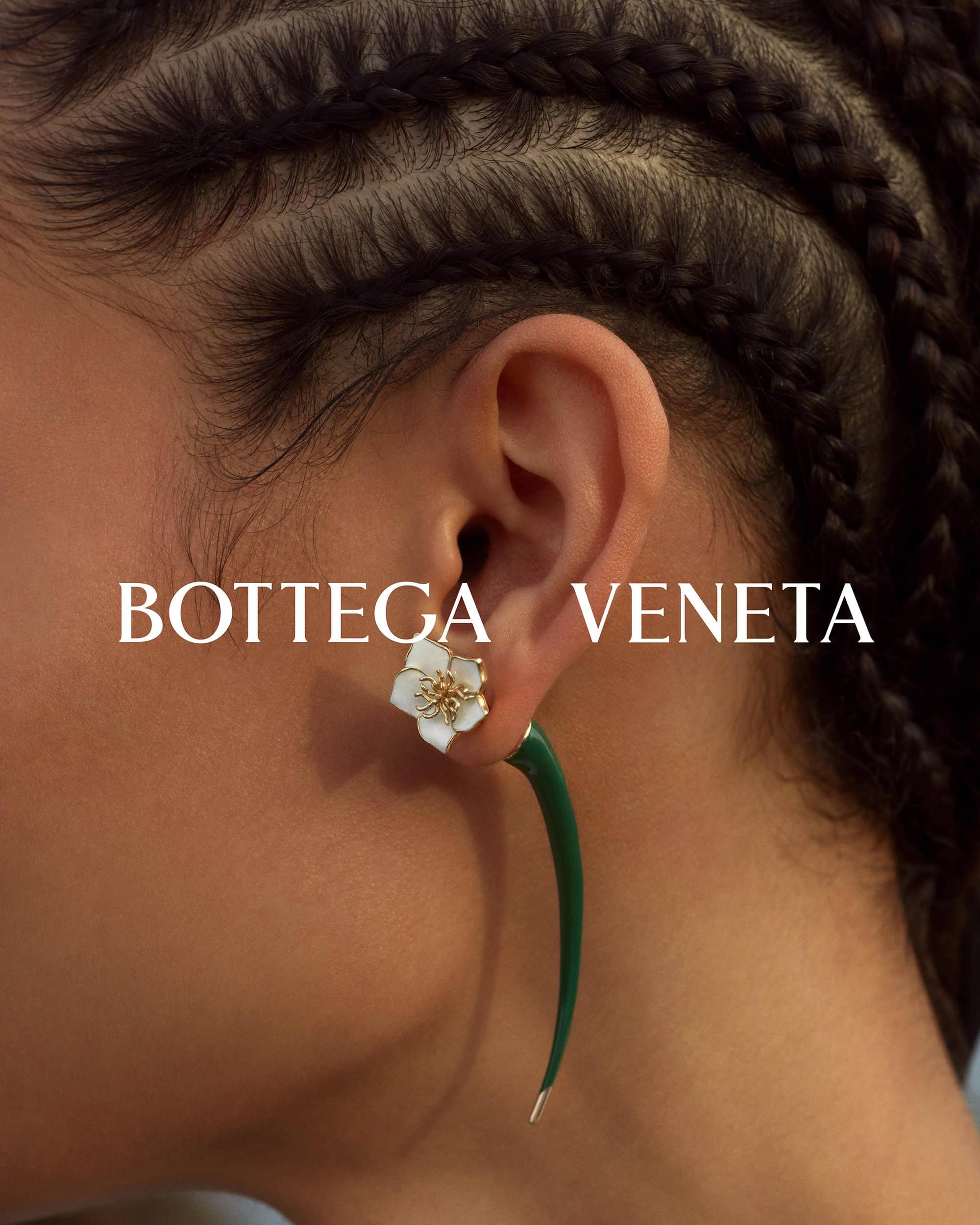 Close-up of a dark-haired person with braided hair wearing a Bottega Veneta flower earring, with a long curved spike and gold stud.