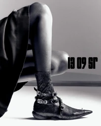 Close-up of a model wearing buckled leather boots and a dark skirt against a minimal grey and white studio backdrop