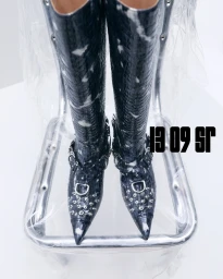 Close-up shot of black crocodile-embossed leather boots with silver studs and buckles resting on a chair