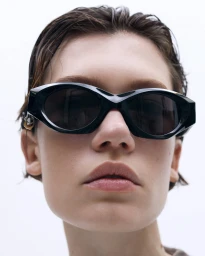 Close-up portrait of a model wearing dark sunglasses with wet-look hair against a plain white background for 13 09 SR.