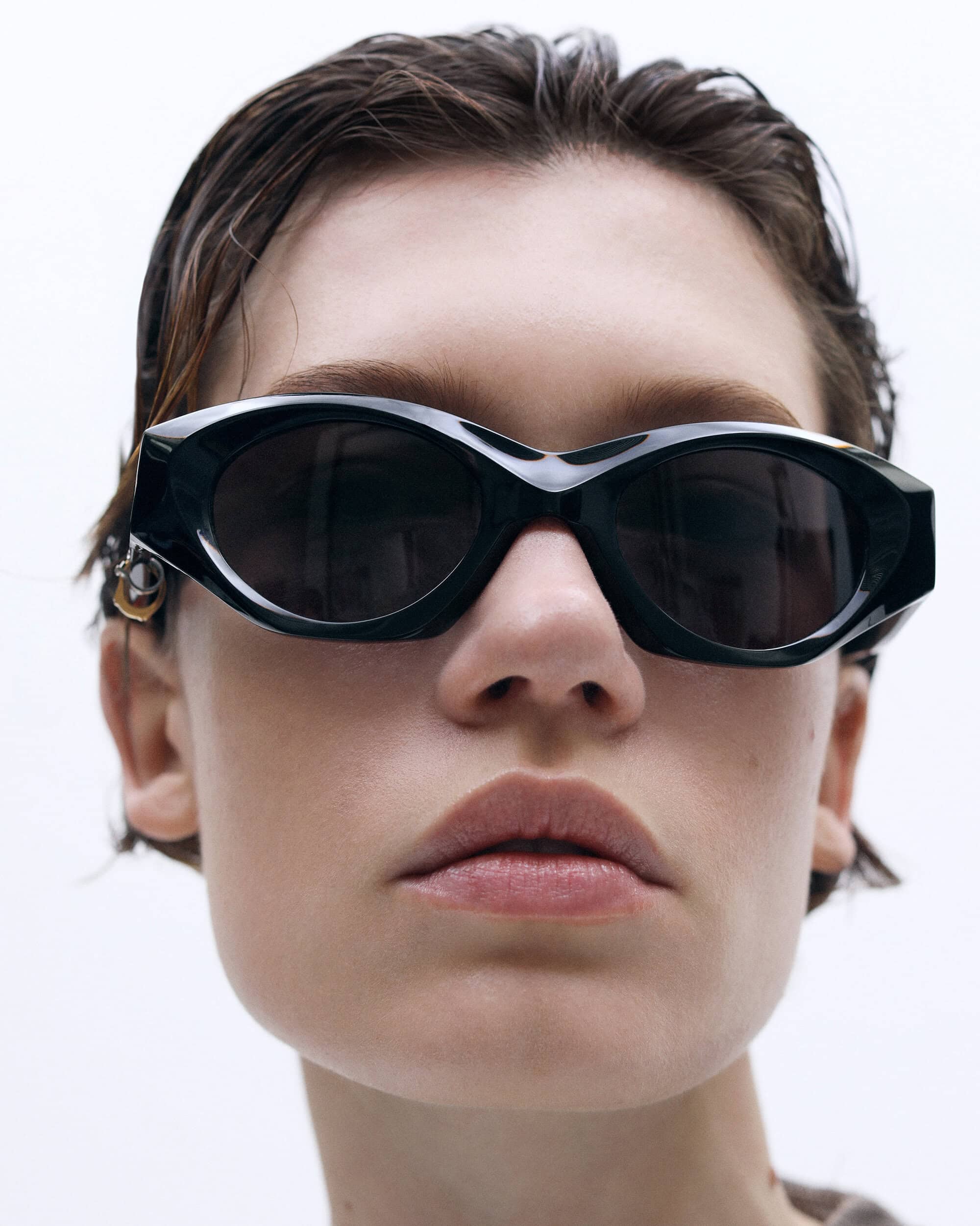 Close-up portrait of a model wearing dark sunglasses with wet-look hair against a plain white background for 13 09 SR.