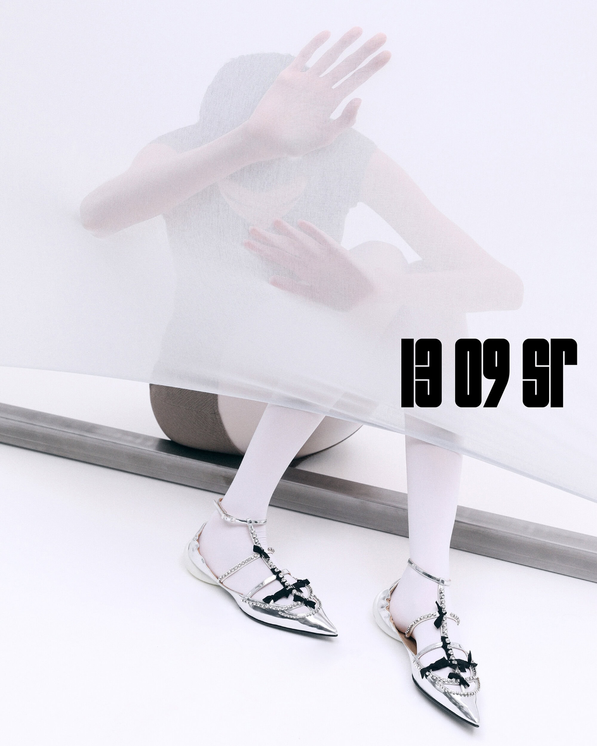 Fashion-forward editorial shot showcasing silver pointy flats with embellished straps, styled with white tights in a bright, minimalist setting.
