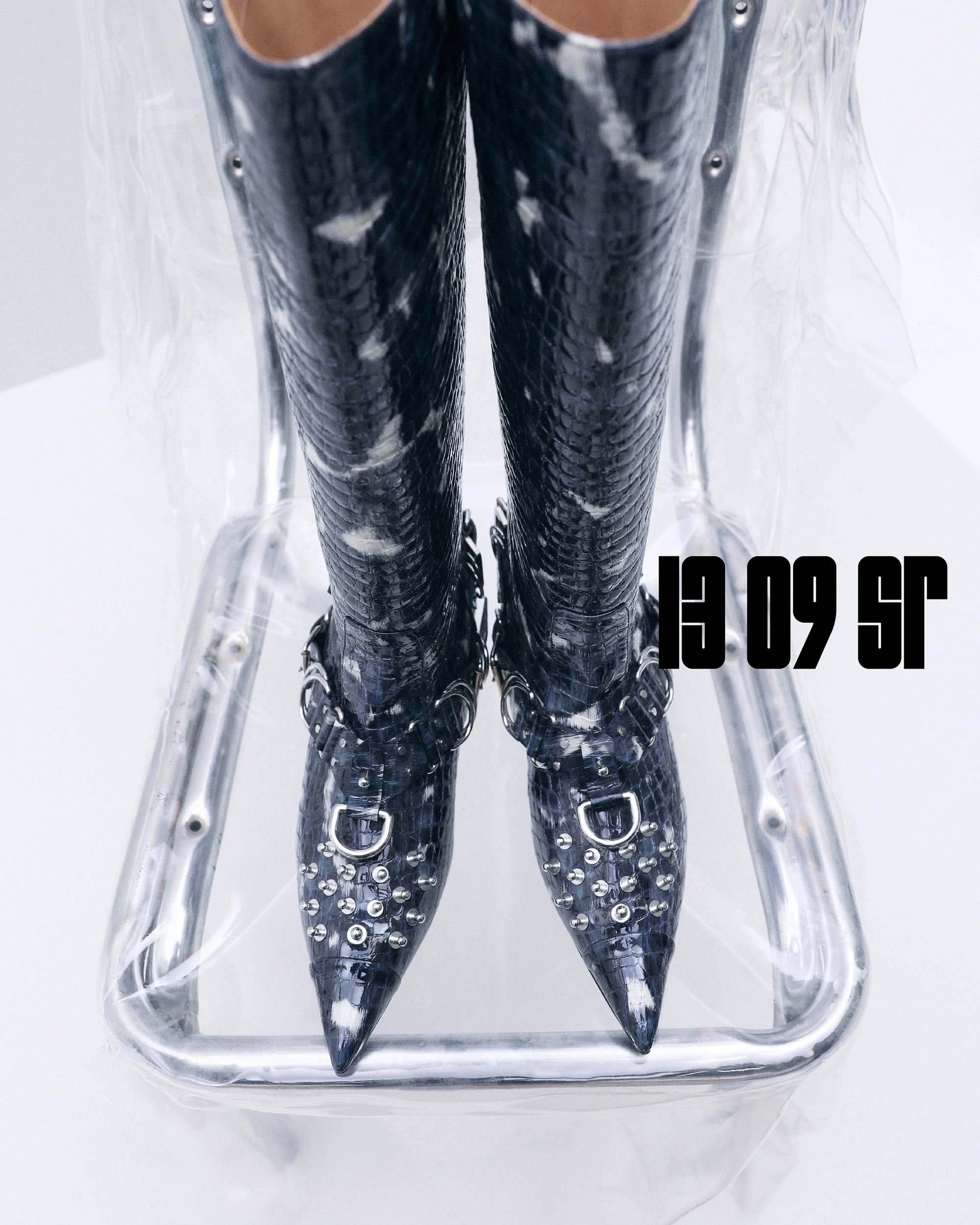 Striking black and white reptile-patterned thigh-high boots with silver studs on a reflective chrome chair against a minimalist background.