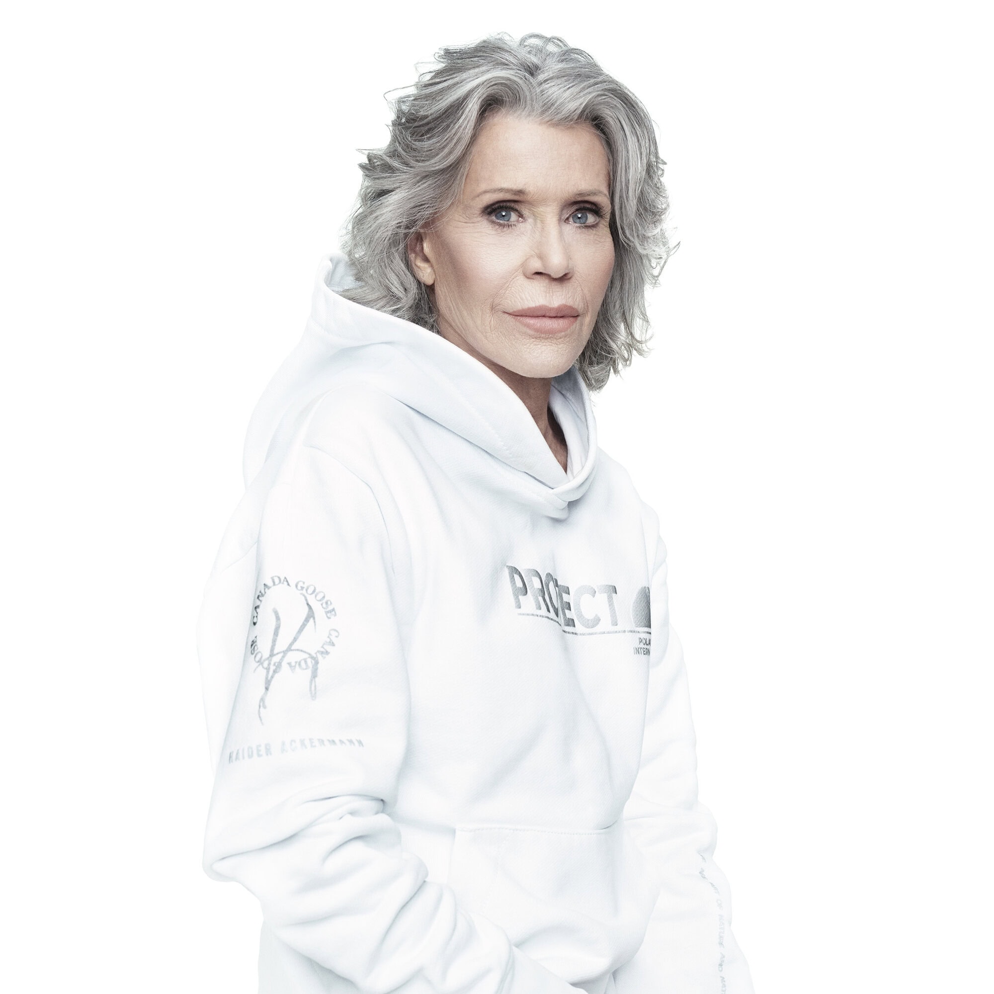 Headshot of Jane Fonda looking directly at the camera. She wears a white hoodie with grey hair against a bright white background.