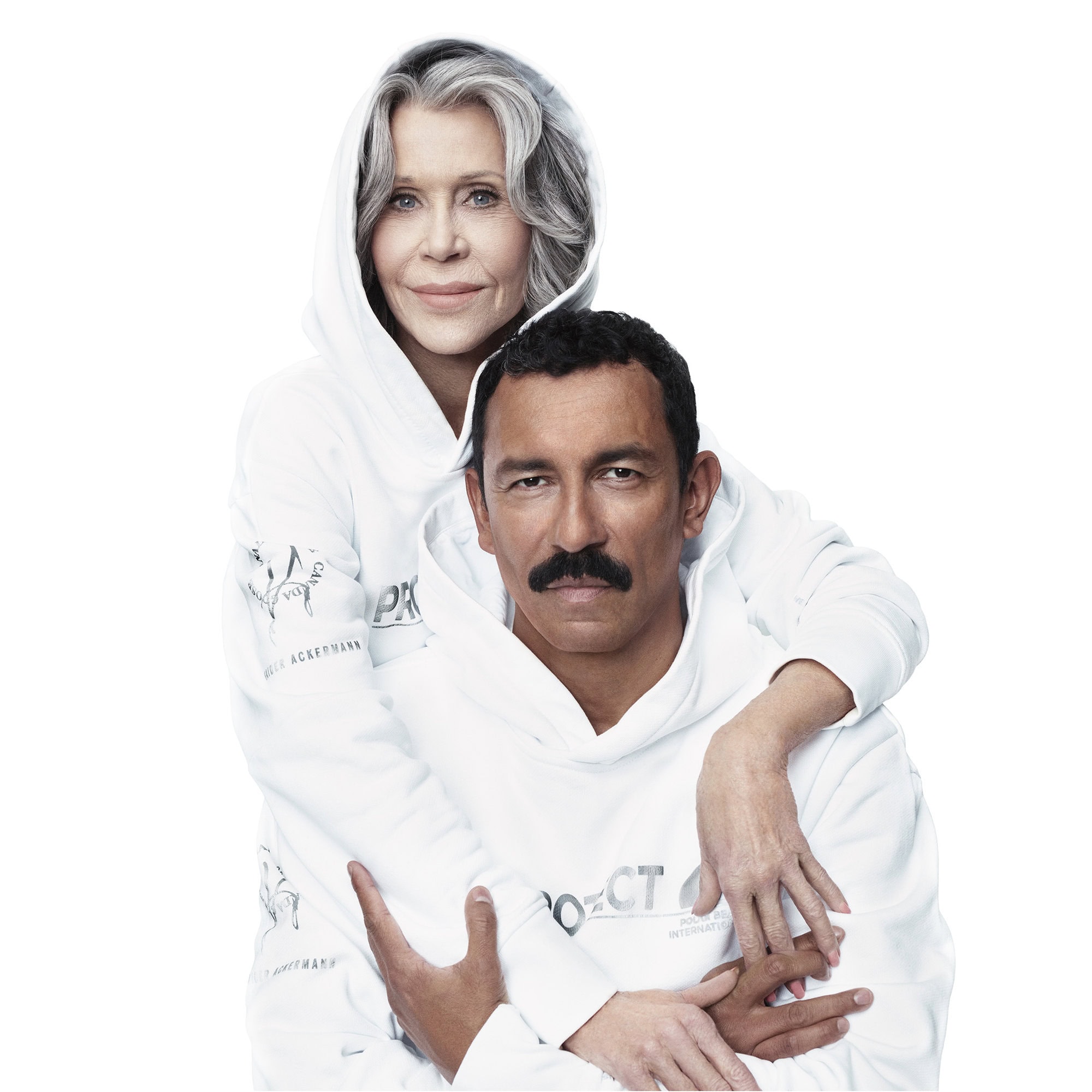 Two people pose in white hooded sweatshirts. An older woman is behind a younger man and has her arms around him.
