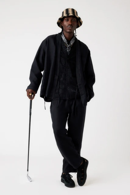 Adult Black male in stylish black suit and striped bucket hat stands with a golf club against a plain background in a studio shot.