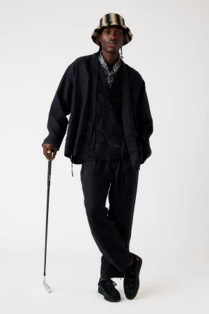 Adult Black male in stylish black suit and striped bucket hat stands with a golf club against a plain background in a studio shot.