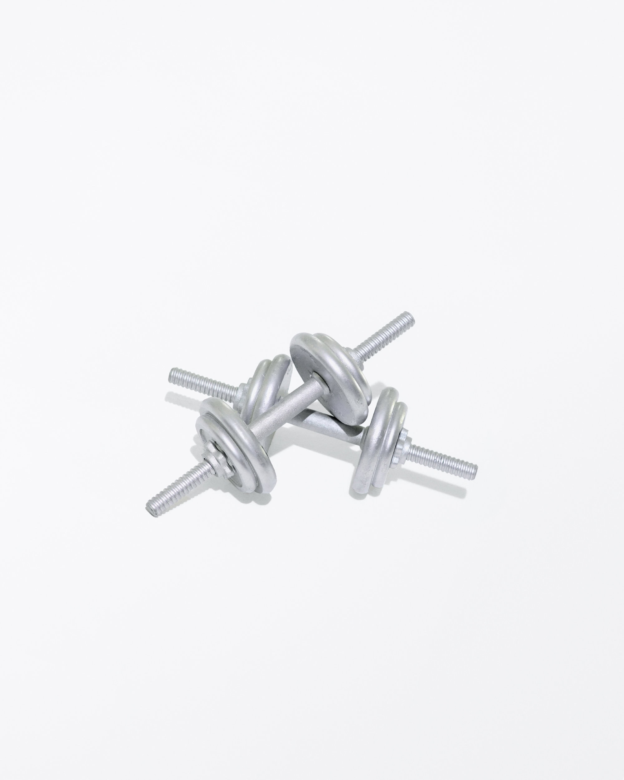 Close-up of two silver dumbbells overlapping on a white surface, ideal for strength training and fitness workouts at the gym.
