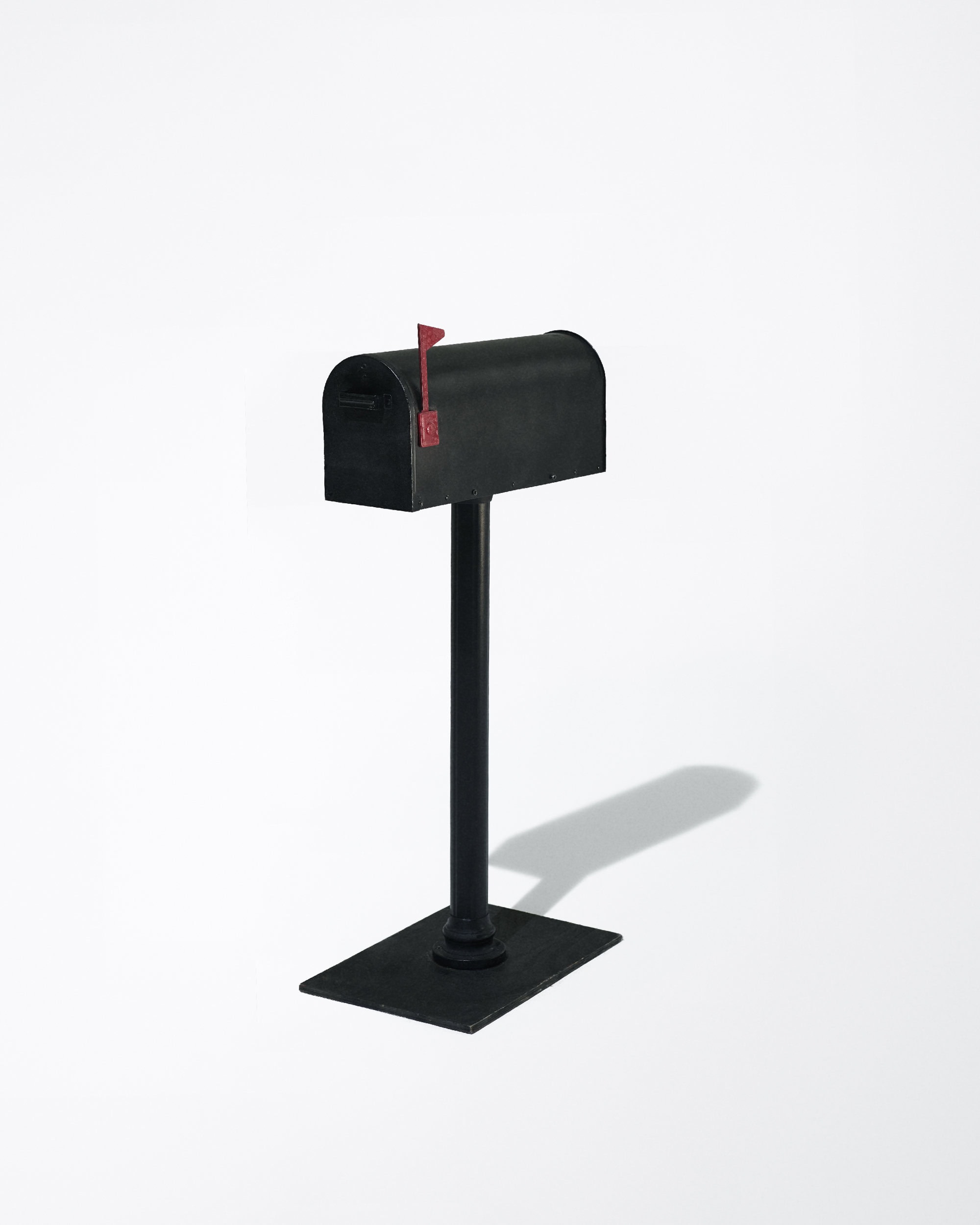 Black mailbox on a stand with a raised red flag against a white background