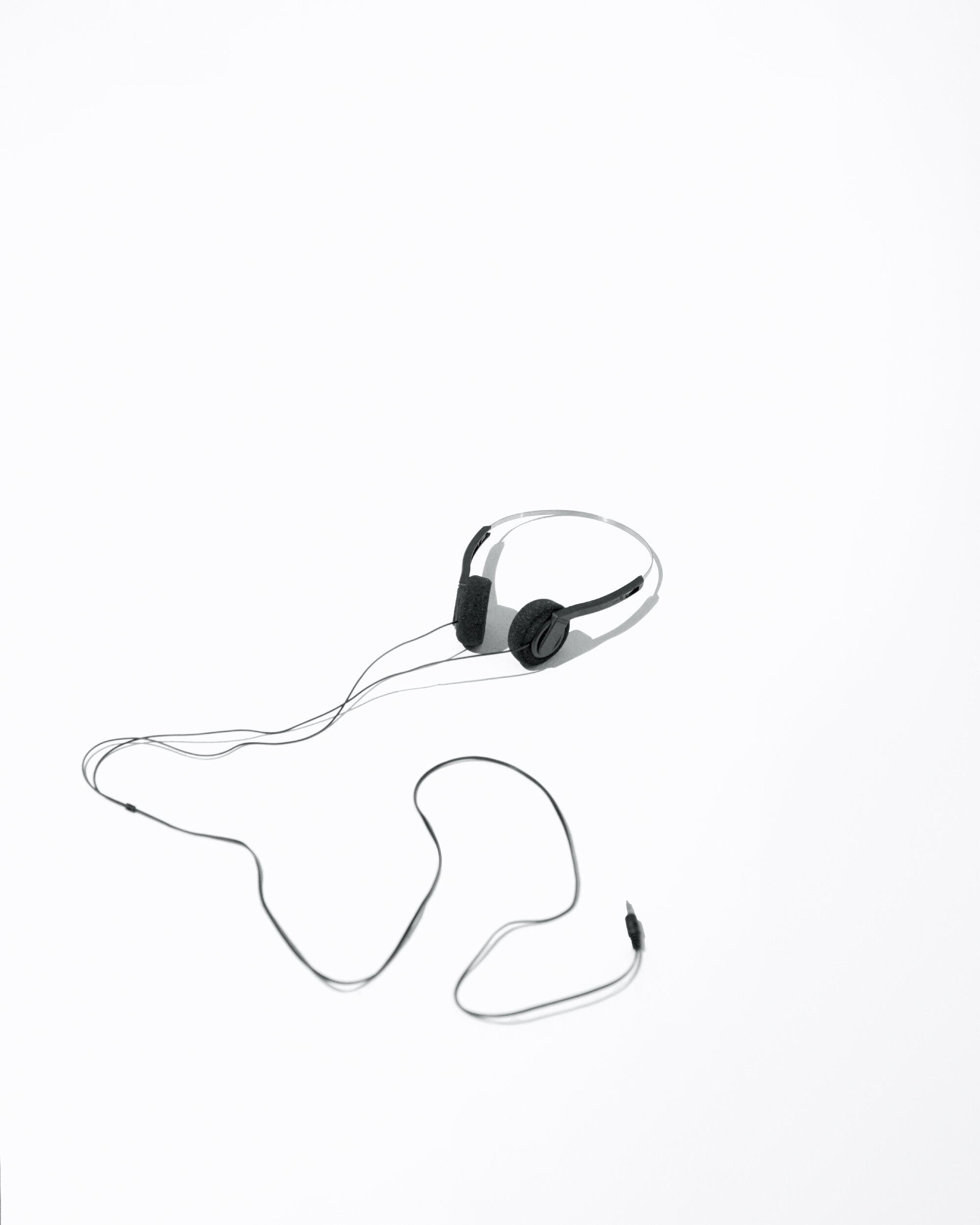 Black wired headphones with attached microphone laying on a bright white surface with long cord stretched out in a studio environment.