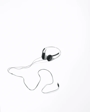 Black wired headphones with attached microphone laying on a bright white surface with long cord stretched out in a studio environment.