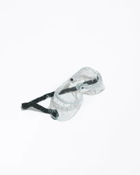 Clear protective safety goggles with a black patterned strap resting diagonally against a seamless white background.