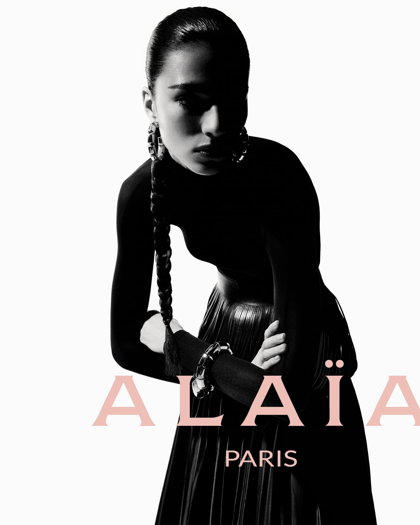 Fashion editorial shot of a woman in a black top and metallic skirt, accessorized with hoop earrings and silver bracelets against a white background.