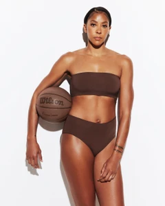 Athletic woman wearing brown two-piece apparel holding a basketball against a plain white studio background.