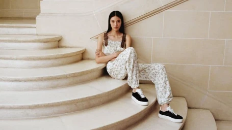 Model seated on stone staircase wearing patterned top and trousers with sneakers