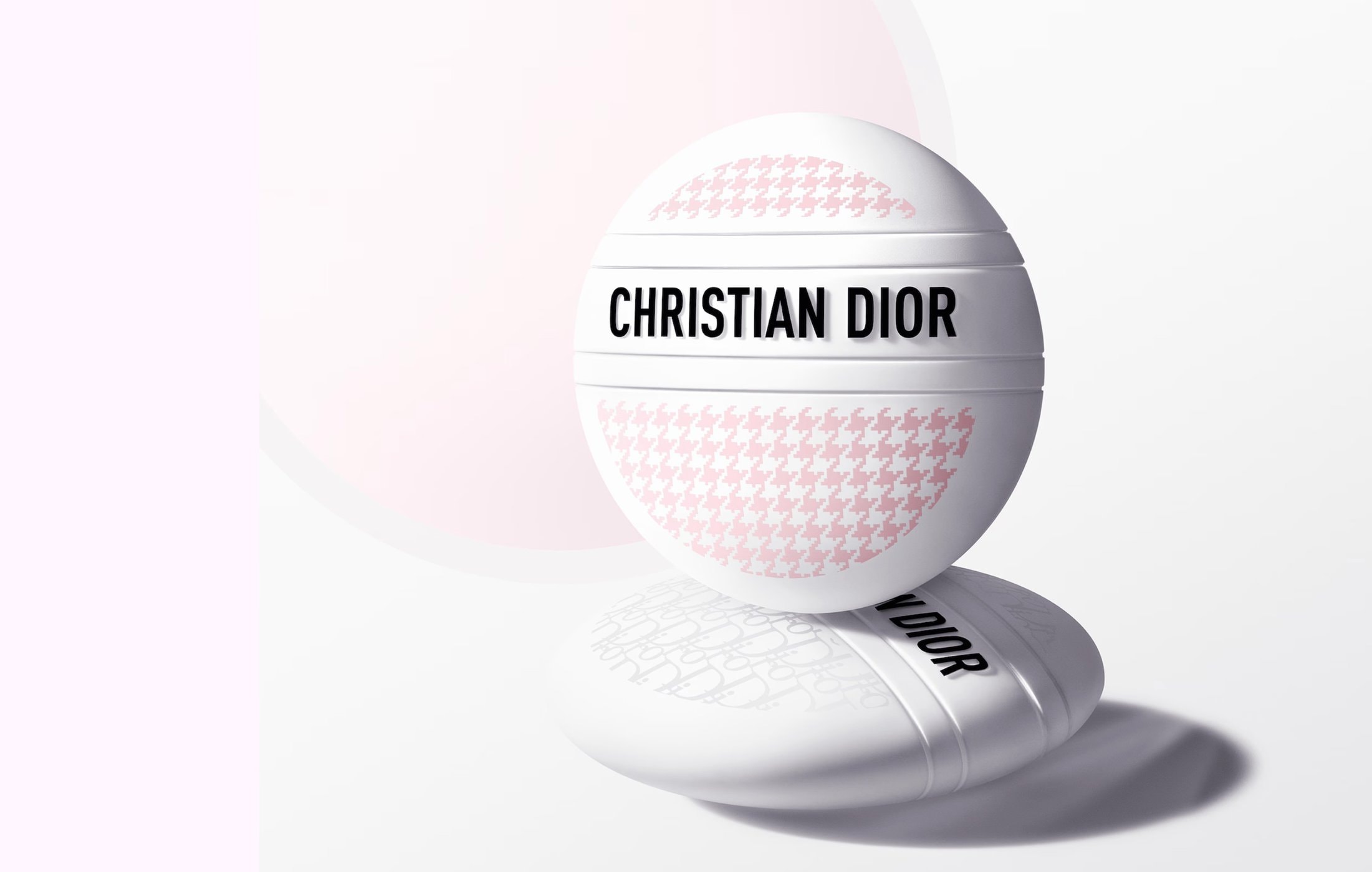 Close-up of a Christian Dior beauty product: A round compact with houndstooth pattern sits on a base against a soft gradient background.