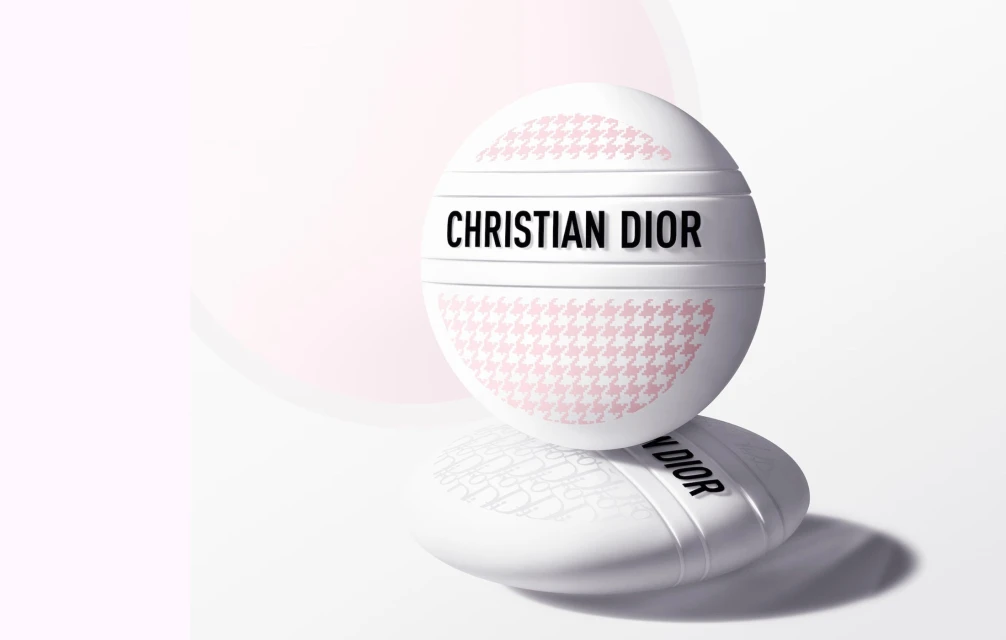 Close-up of a Christian Dior beauty product: A round compact with houndstooth pattern sits on a base against a soft gradient background.