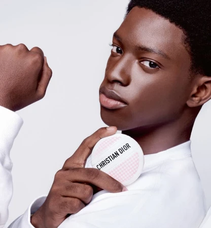 Close-up of a young adult Black male model holding a Christian Dior makeup compact, showcasing beauty and fashion in a clean photo studio setting.