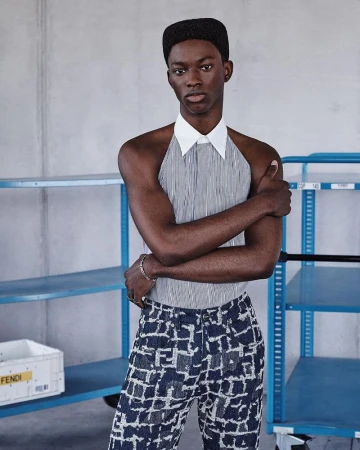 Stylish young adult in collared halter top and Fendi patterned pants poses indoors in front of shelving with labeled storage box.
