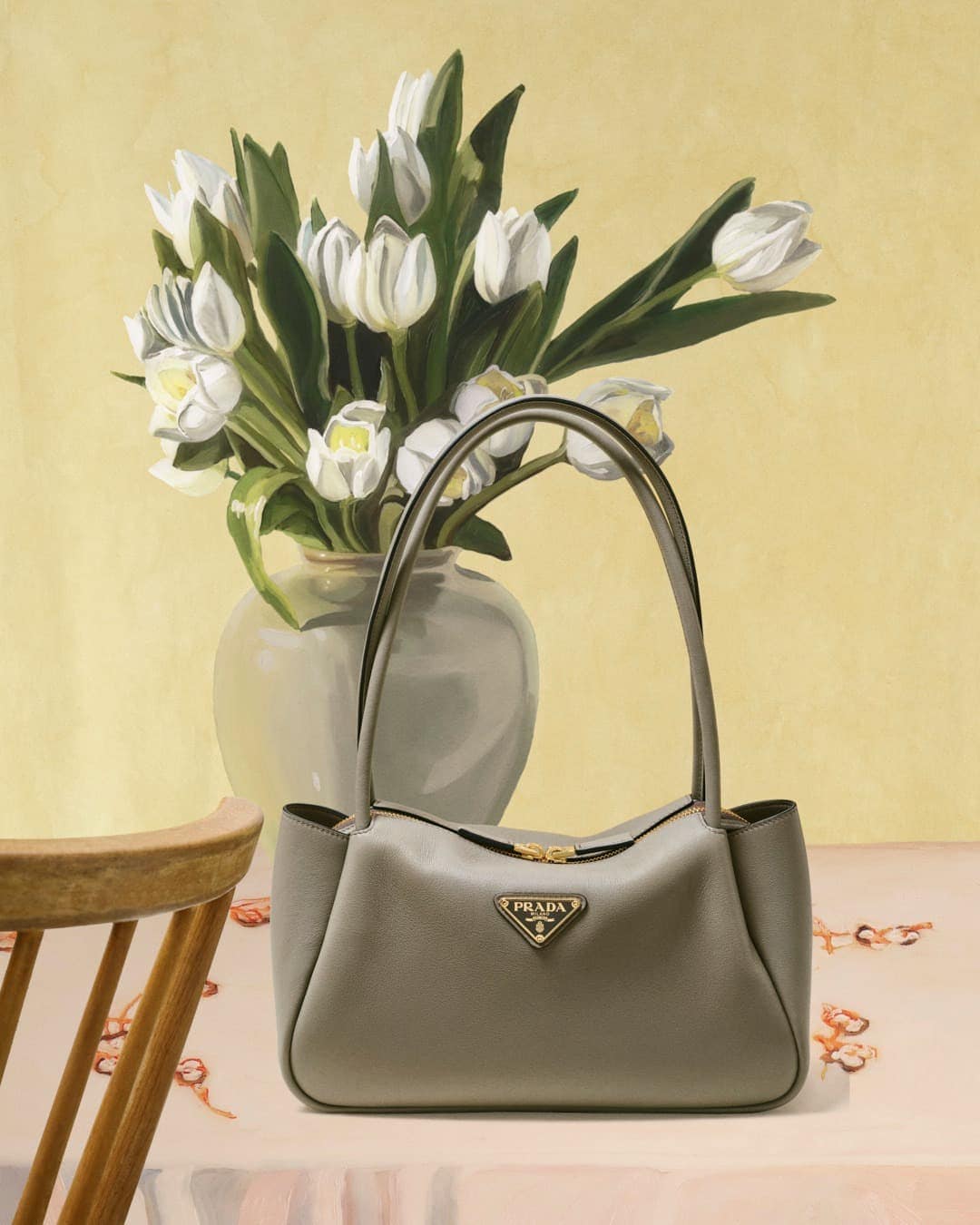 Still life painting of a Prada bag in front of white tulips in a vase, displayed on a draped table with a chair in the frame.