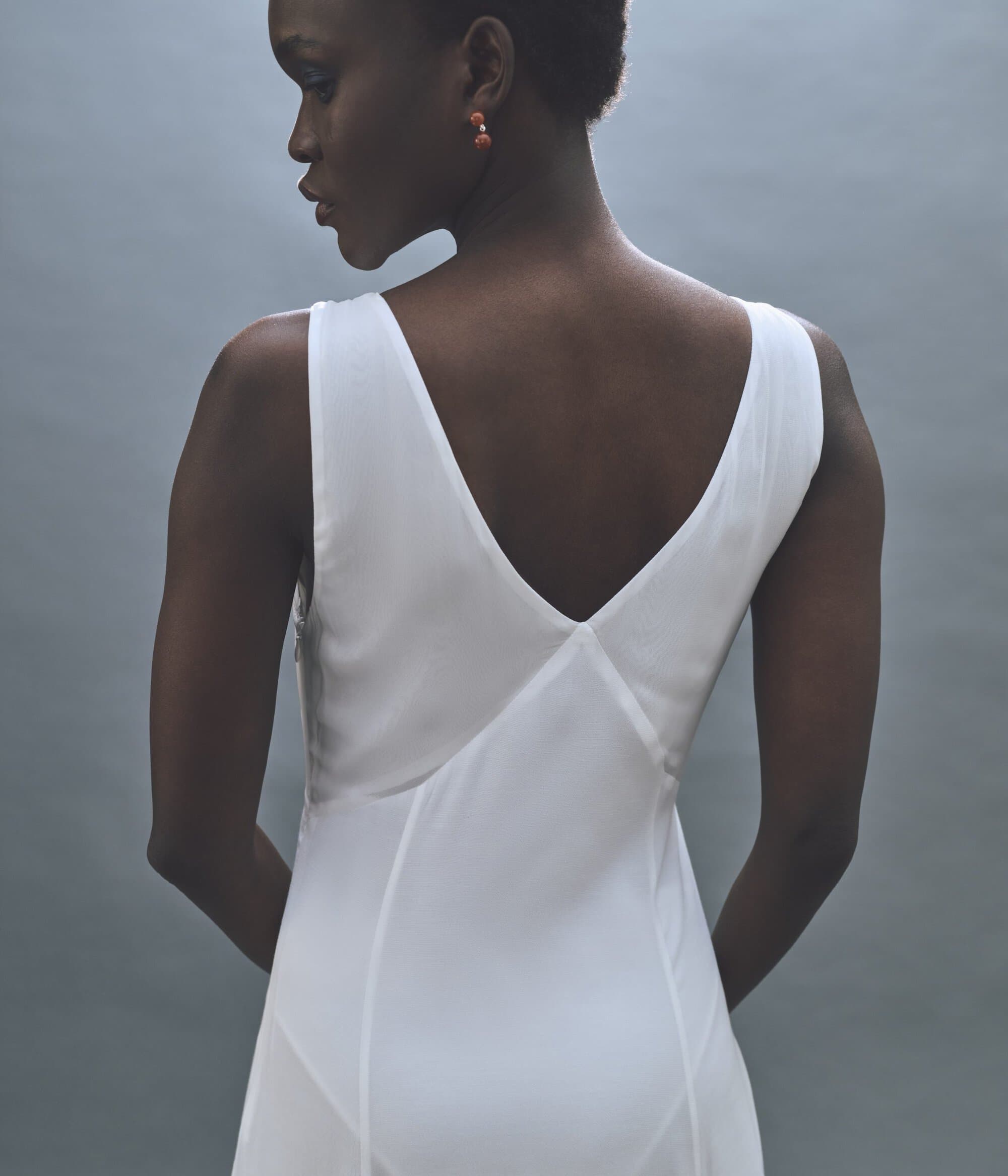 Model seen from behind wearing a white v-neck slip dress against a neutral grey studio backdrop for Rue Sophie.