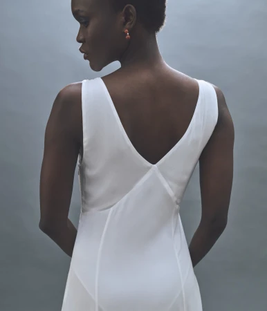 Model seen from behind wearing a white v-neck slip dress against a neutral grey studio backdrop for Rue Sophie.