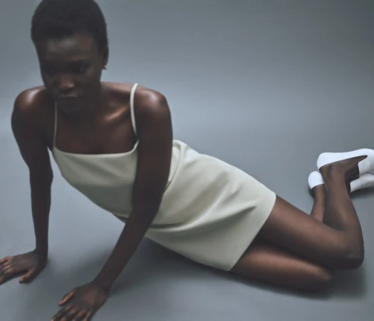 Model in cream slip dress and white shoes leaning on grey studio floor for Rue Sophie Summer 2024 campaign