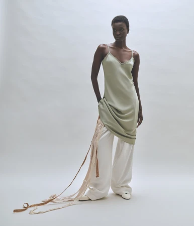 Model wearing a sage green slip dress and white trousers against a neutral background for Rue Sophie.