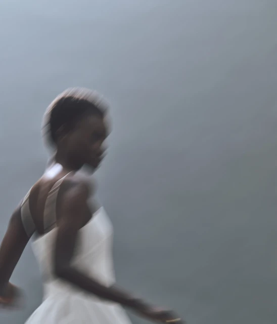 Motion blur of a Black woman in a light dress against a grey background, creating an abstract and dynamic fashion image.